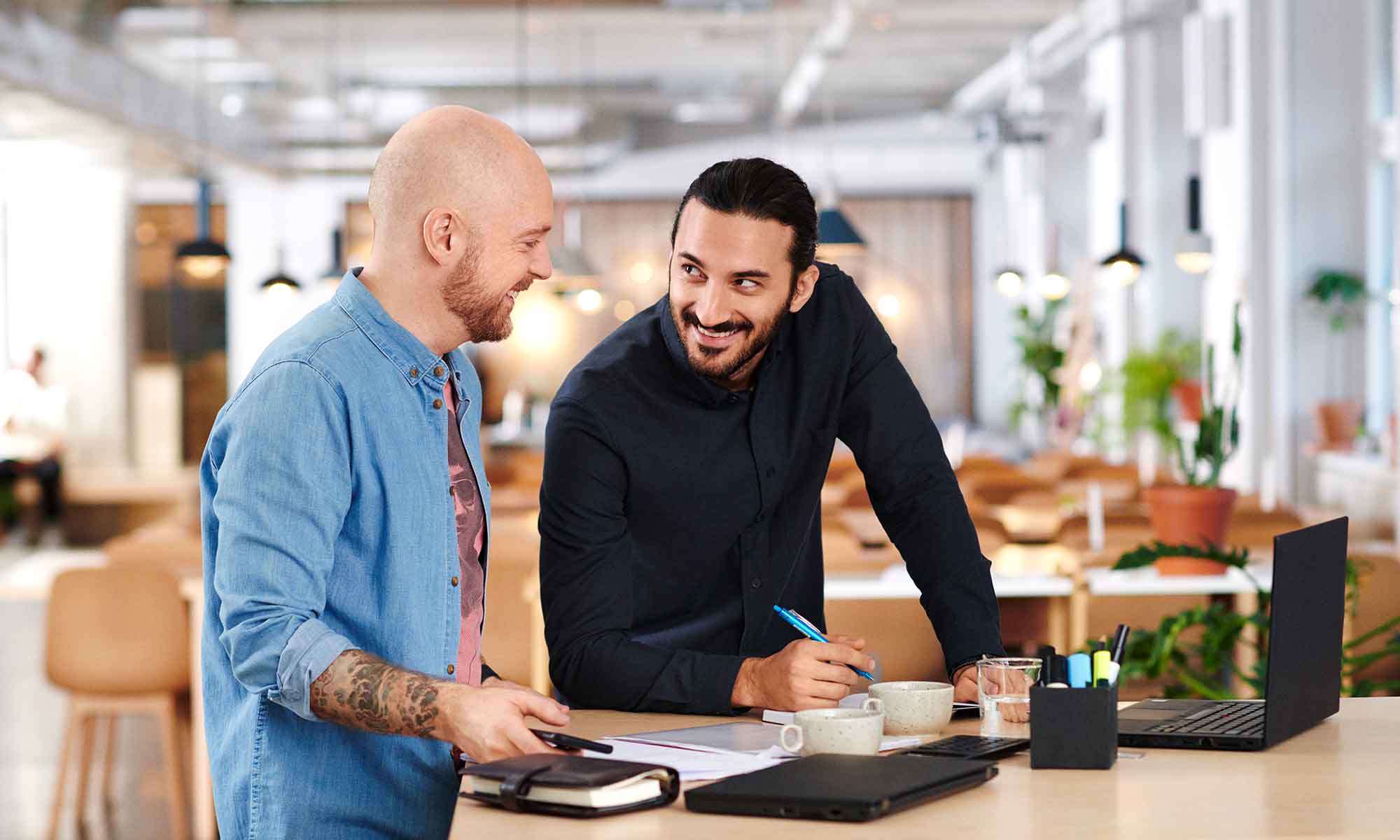 Två glada män på en arbetsplats står vid ett skrivbord och jobbar